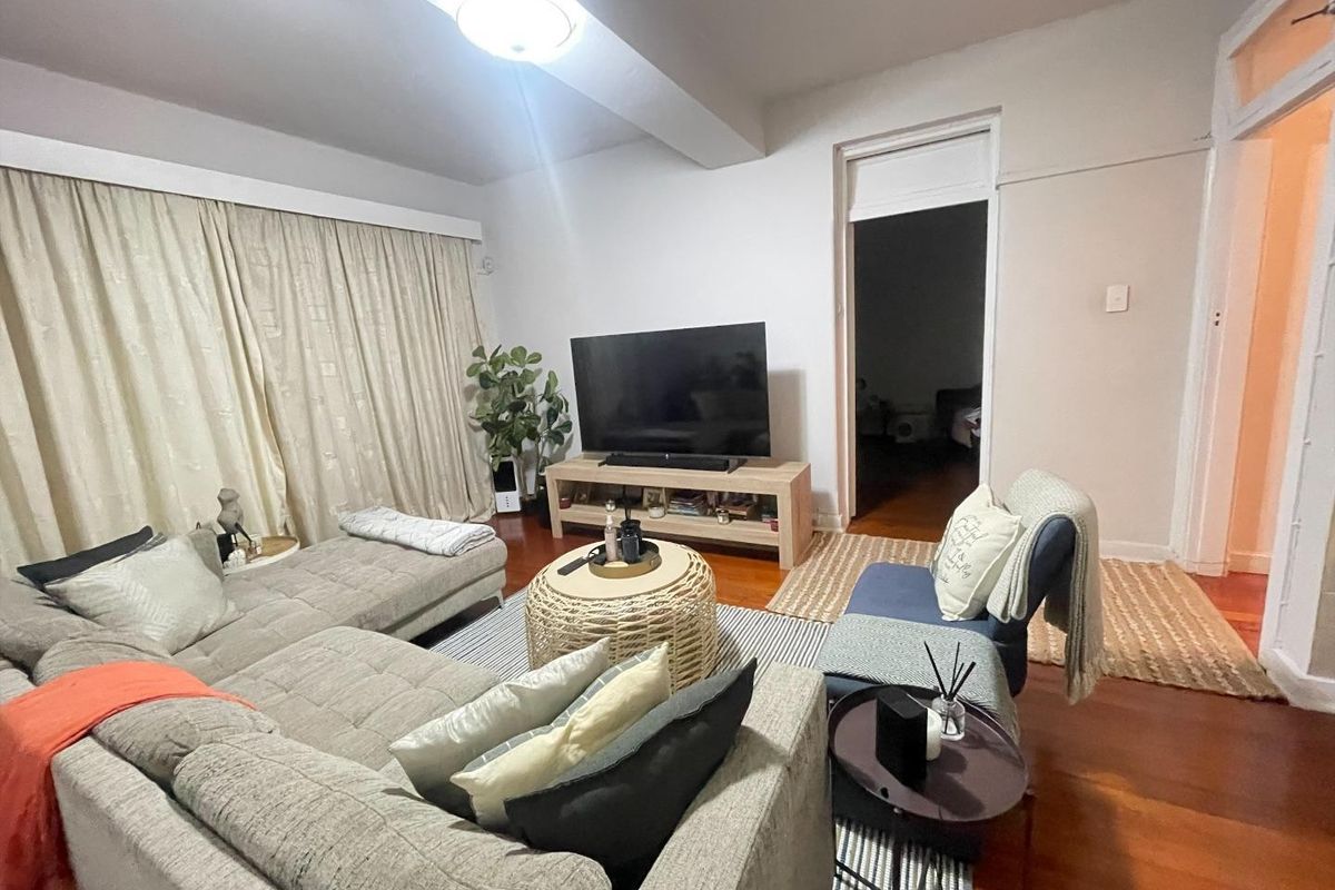 A comfortable living room featuring warm hardwood flooring and large window curtains, providing a cozy and inviting atmosphere for relaxation.