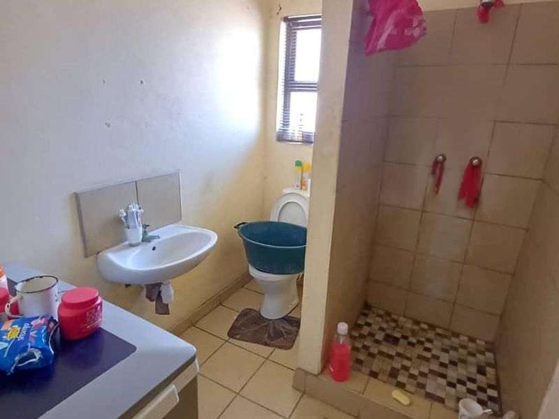 A functional bathroom featuring a wall-mounted basin, toilet, and a tiled shower enclosure with basic finishes.