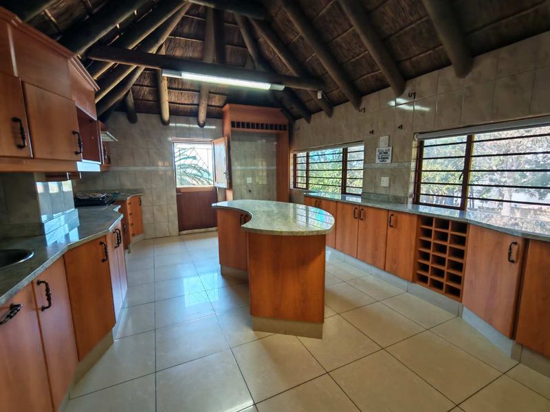 Spacious kitchen featuring wooden cabinetry, granite countertops, a central island, and a unique vaulted thatch ceiling with exposed timber beams.