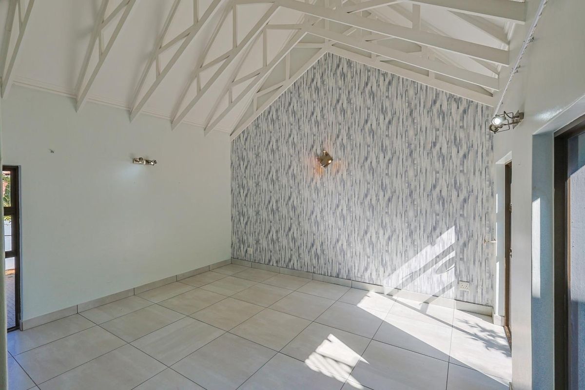 A bright, empty living room featuring high vaulted ceilings with exposed trusses, tiled flooring, and a decorative feature wall.
