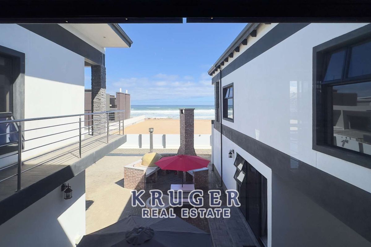 Outdoor courtyard area featuring a built-in brick braai and pizza oven, situated between two modern residential structures with direct beach and ocean views.