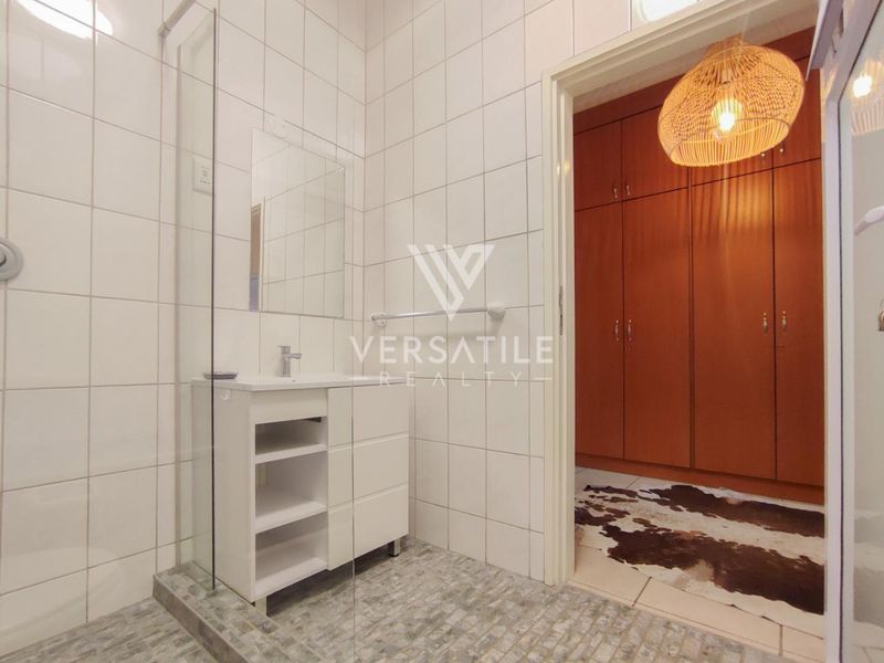 A modern bathroom featuring a glass-enclosed shower, vanity unit, and tiled finishes, with adjacent built-in storage cupboards.