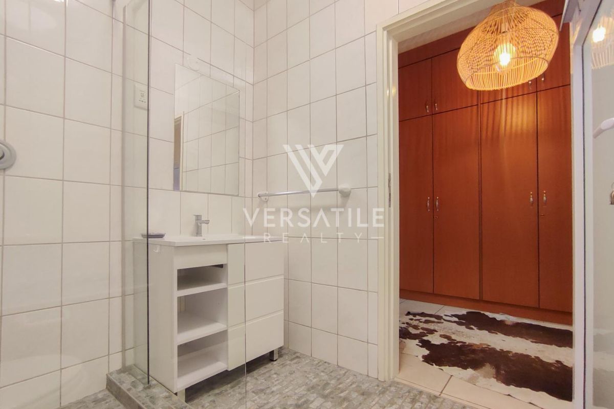 A modern bathroom featuring a glass-enclosed shower, vanity unit, and tiled finishes, with adjacent built-in storage cupboards.