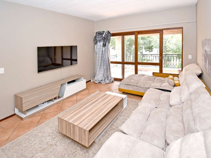 A comfortable living room featuring terracotta floor tiles, a drop ceiling, and large sliding glass doors providing access to an outdoor balcony area.