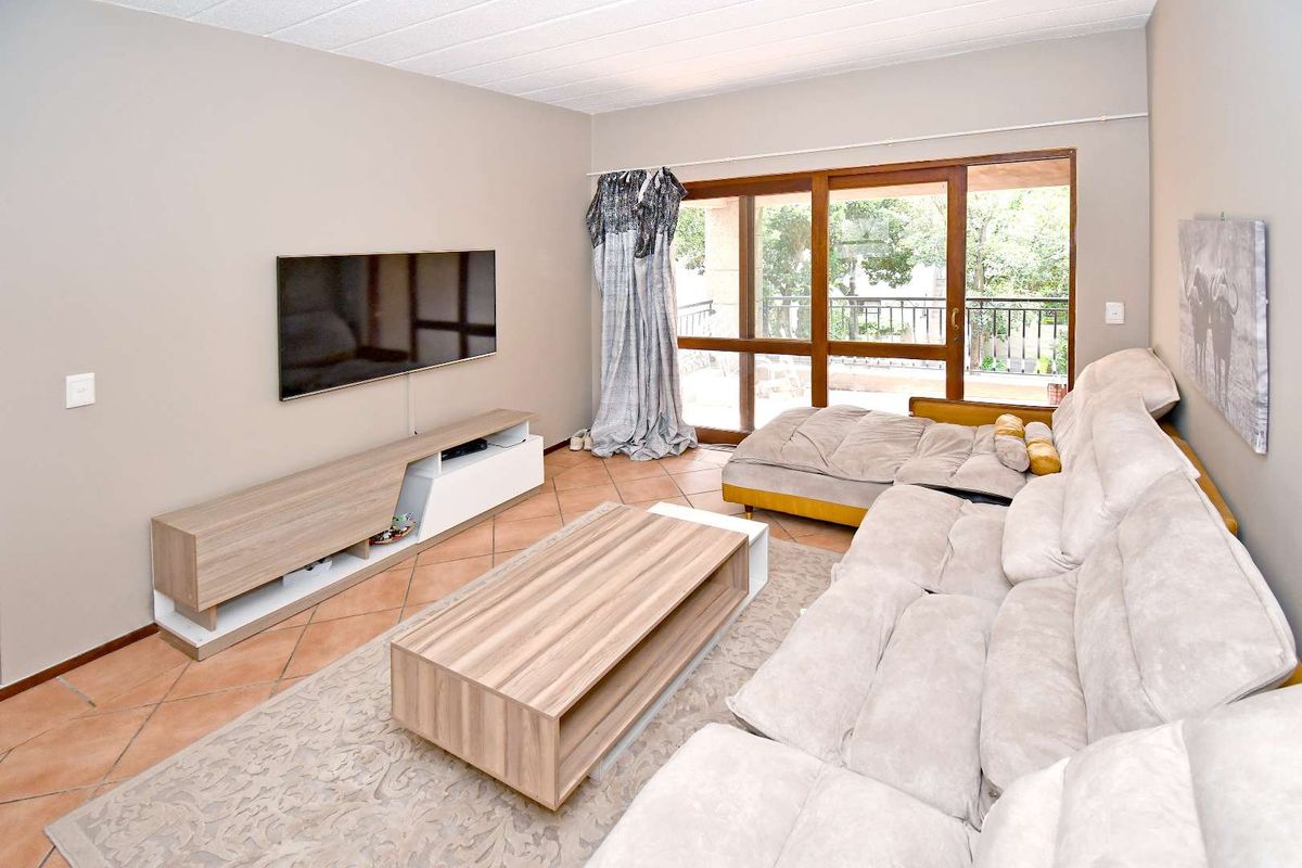 A comfortable living room featuring terracotta floor tiles, a drop ceiling, and large sliding glass doors providing access to an outdoor balcony area.