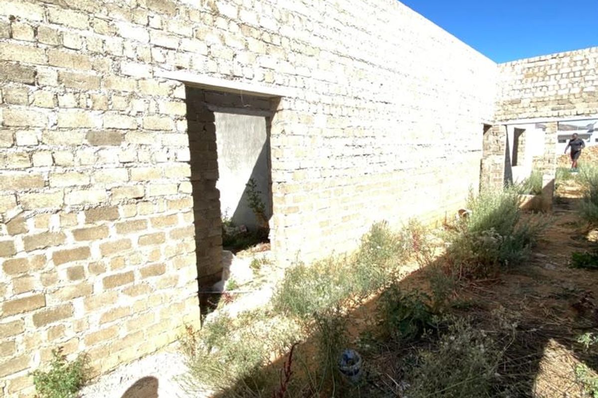 An unfinished exterior view of a property under construction, featuring exposed brick walls and open doorways in a shell state.