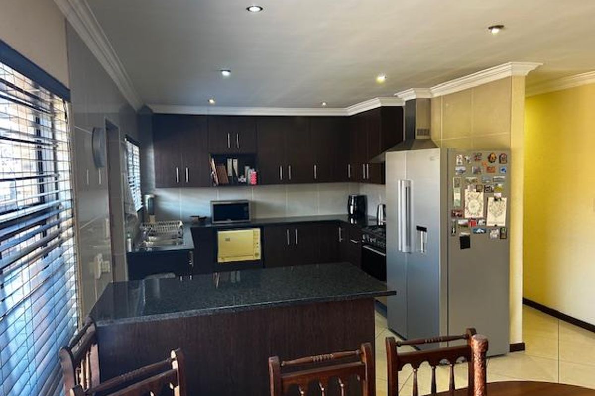 A functional kitchen featuring dark wood cabinetry, granite countertops, a breakfast nook, and built-in stainless steel appliances including an extractor fan.