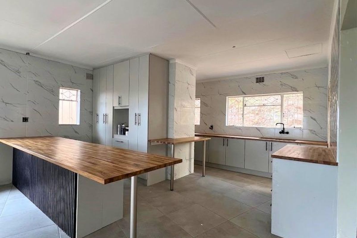Modern kitchen featuring marble-look wall cladding, timber-style countertops, a central island with breakfast bar, and ample built-in cabinetry.