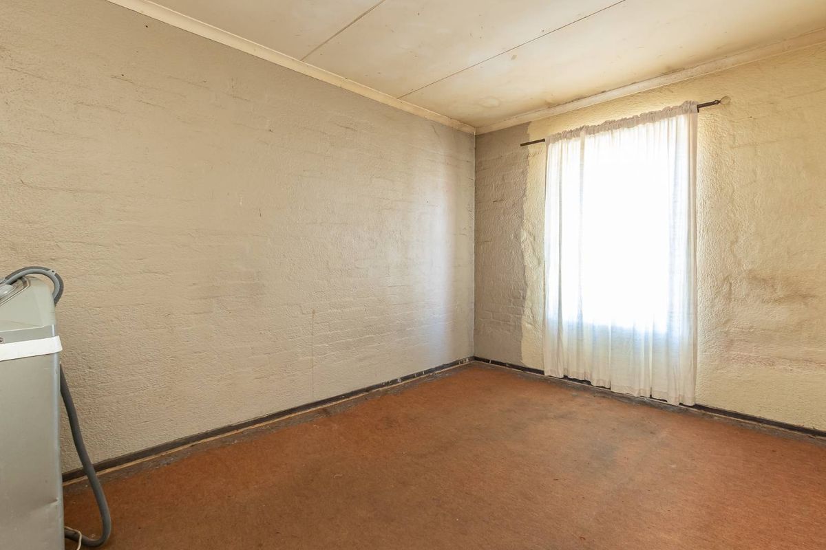 An empty bedroom featuring textured walls, a single window with curtain, and worn flooring, presenting a blank canvas for renovation.