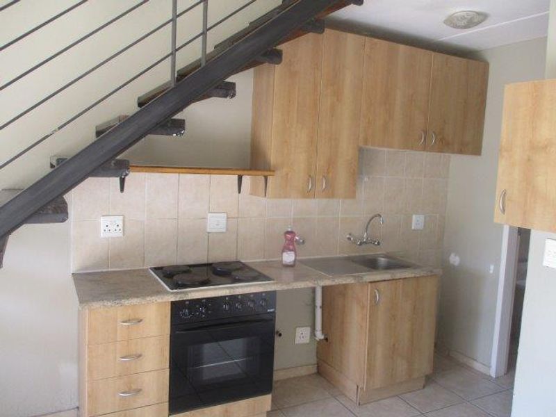 Compact kitchen featuring light wood cabinetry, built-in oven and hob, tiled backsplash, and an integrated staircase, requiring minor cosmetic updates.