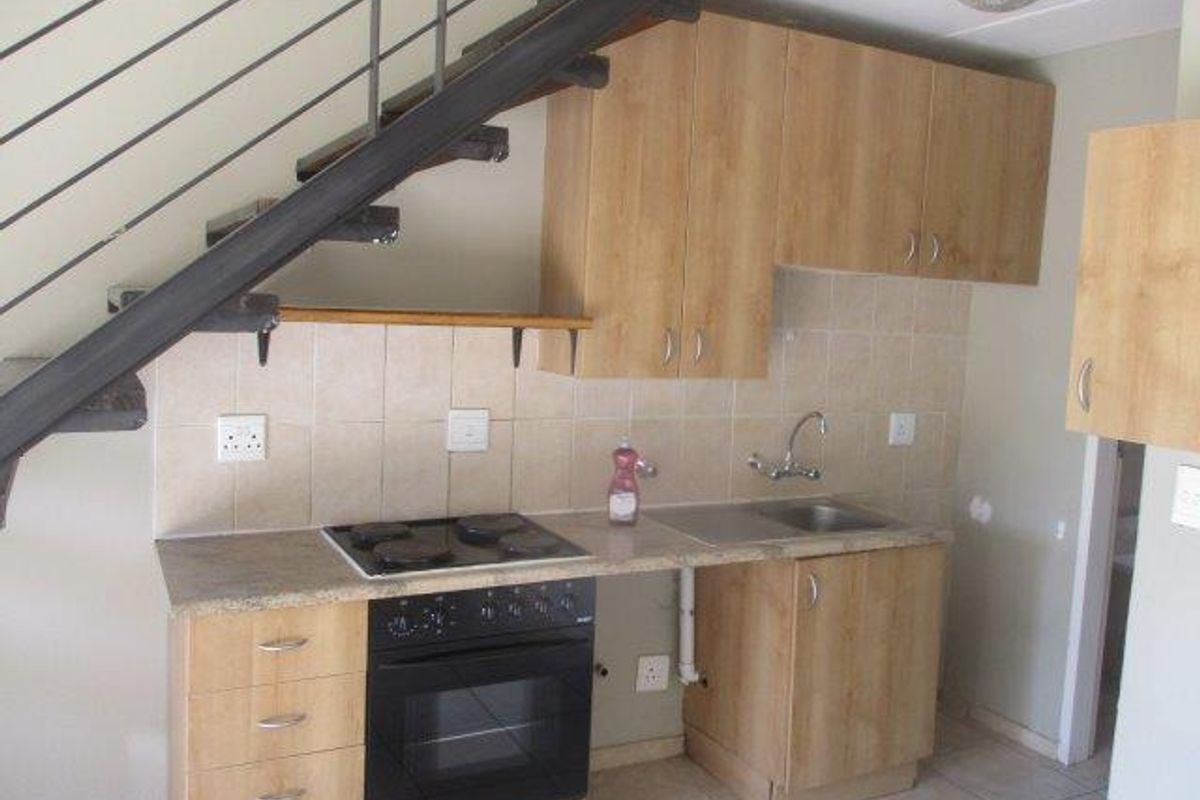 Compact kitchen featuring light wood cabinetry, built-in oven and hob, tiled backsplash, and an integrated staircase, requiring minor cosmetic updates.