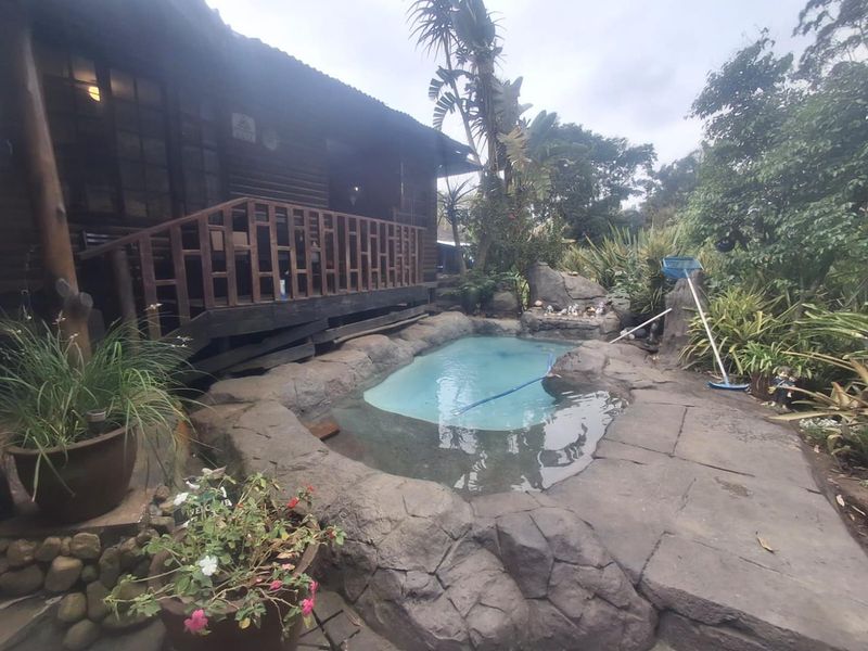 A rustic cottage exterior featuring a naturalistic rock-style swimming pool and an elevated timber deck area.