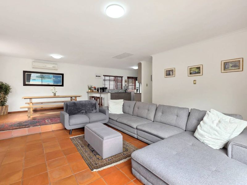 Spacious open-plan living and dining area featuring terracotta tiled flooring, split-system air conditioning, and a functional kitchen layout with neutral finishes.