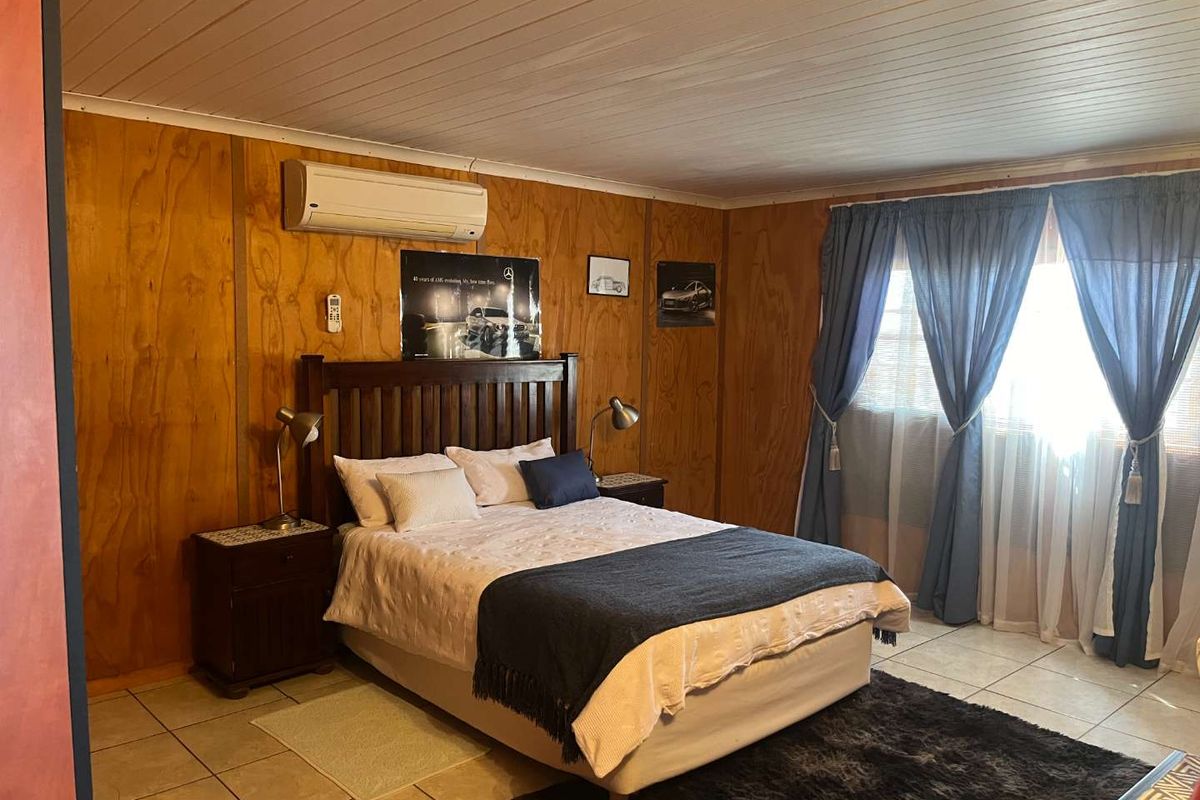 A bedroom featuring wood-paneled walls, tiled flooring, and a wall-mounted air conditioning unit.