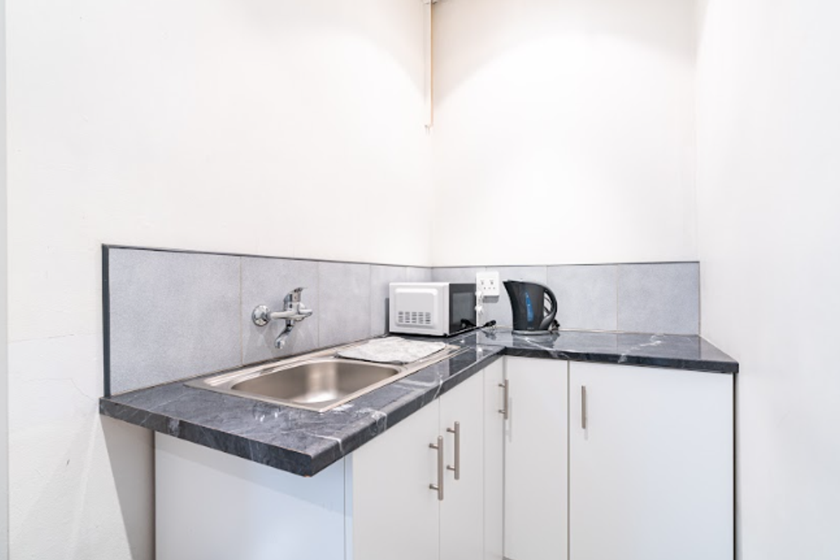 A compact kitchenette featuring a stainless steel sink, dark marble-effect laminate countertops, tiled backsplash, and white base cabinetry.