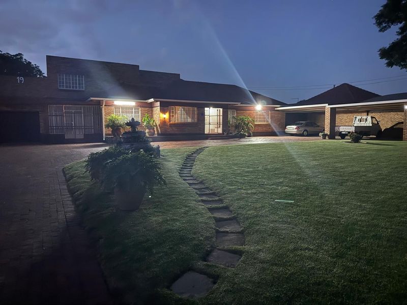 A well-maintained brick house exterior at dusk, featuring a spacious paved driveway, attached carport, landscaped lawn, and stone pathway leading to the entrance.