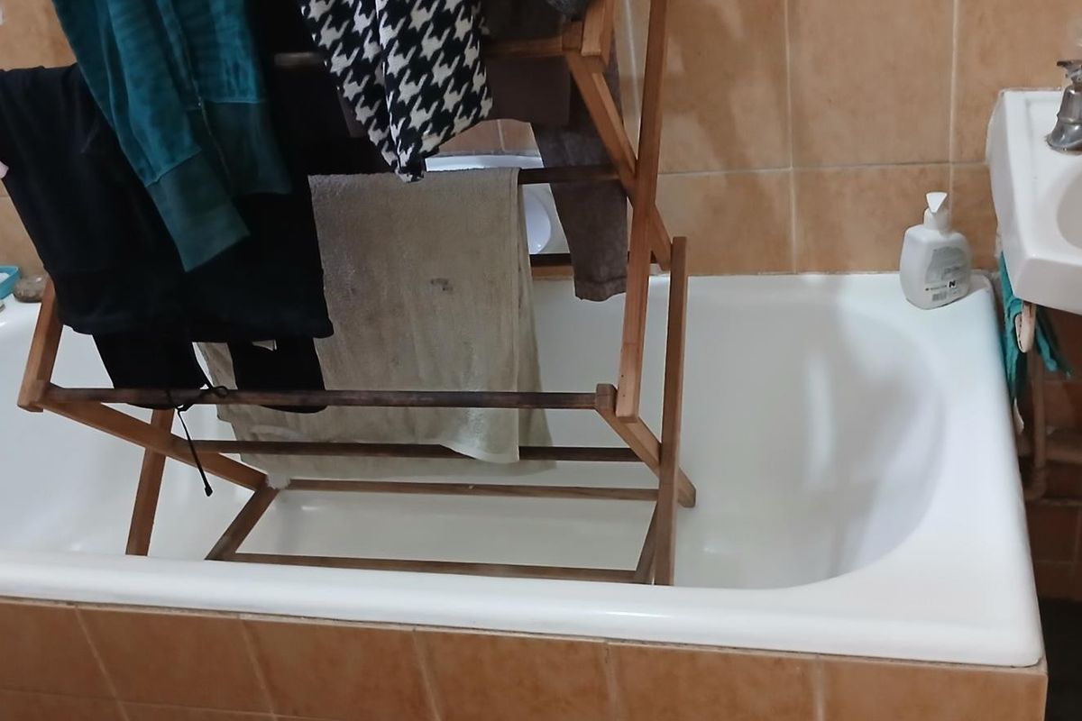 A functional bathroom featuring a standard bathtub, wall-mounted basin, and ceramic wall tiling, currently showing signs of wear and missing base tiles.