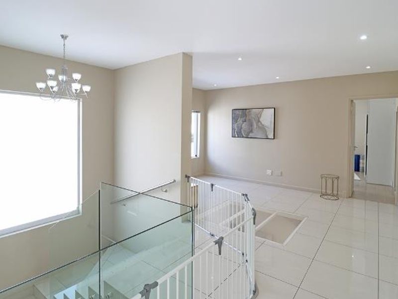 A bright and spacious landing area featuring modern tiled flooring, a glass balustrade, and elegant lighting fixtures, providing access to adjacent rooms.