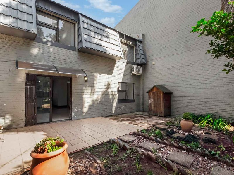 Rear exterior view of the apartment featuring a paved patio area, brick facade, and sliding door access to the interior.