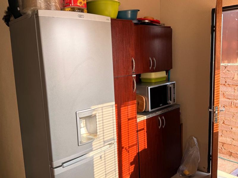 A compact scullery area featuring built-in wooden cabinetry, a built-in microwave, and tiled flooring, with direct access to an outdoor space.