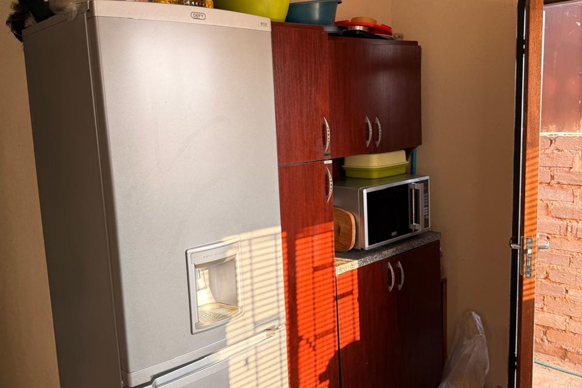 A compact scullery area featuring built-in wooden cabinetry, a built-in microwave, and tiled flooring, with direct access to an outdoor space.