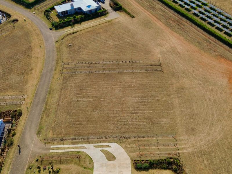 Aerial view of a vacant residential plot featuring a concrete driveway, perimeter fencing, and an established trellis system.