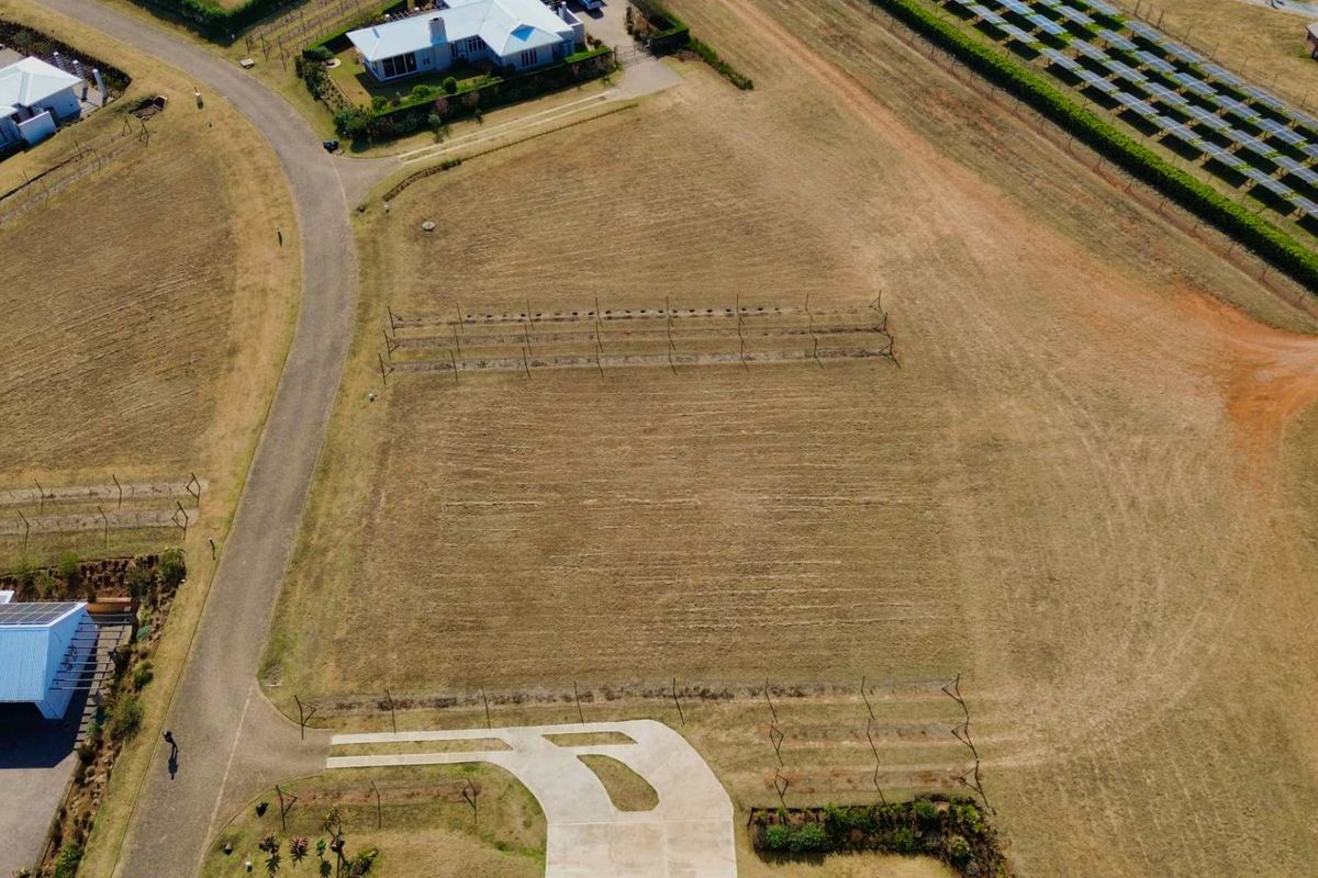 Aerial view of a vacant residential plot featuring a concrete driveway, perimeter fencing, and an established trellis system.