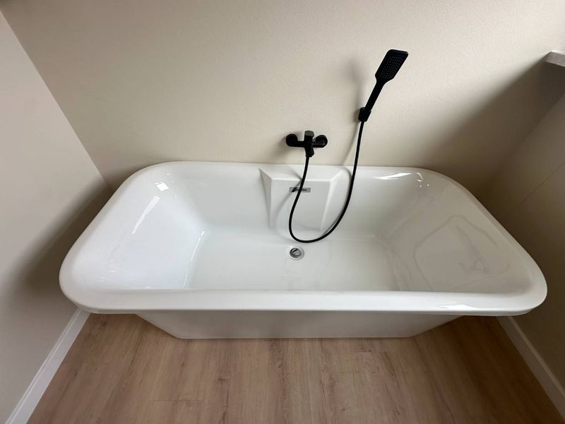 A modern bathroom featuring a clean white freestanding bathtub with contemporary matte black wall-mounted fixtures and durable wood-look laminate flooring.