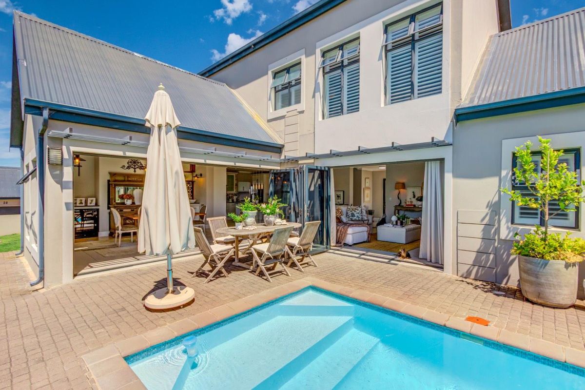 A well-maintained rear courtyard featuring a paved patio area, a swimming pool, and seamless indoor-outdoor flow through large folding doors into the living spaces.