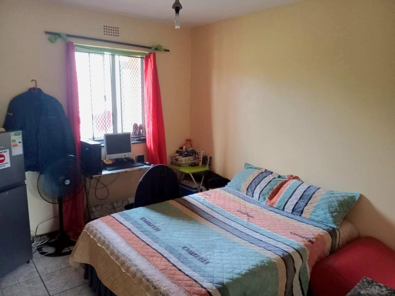 A functional bedroom featuring tiled flooring, a window with security bars, and integrated ventilation brick.