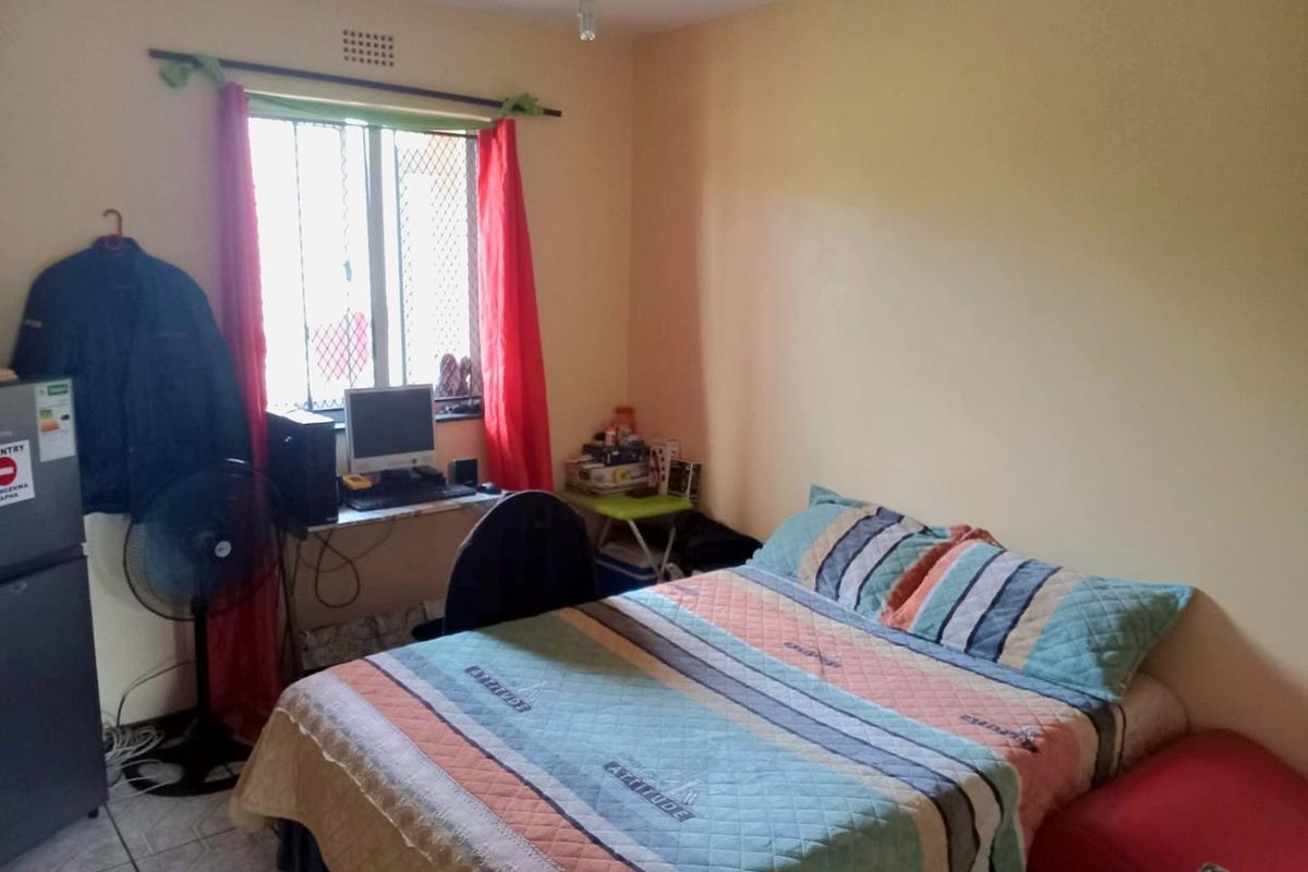 A functional bedroom featuring tiled flooring, a window with security bars, and integrated ventilation brick.