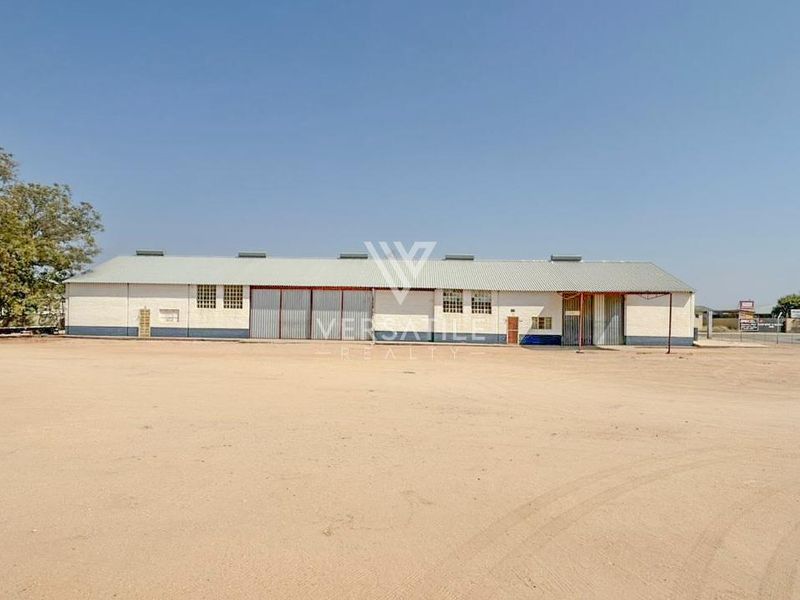 A wide-angle view of a large industrial warehouse building featuring corrugated metal roofing and multiple sliding access doors, set on a spacious dirt lot.