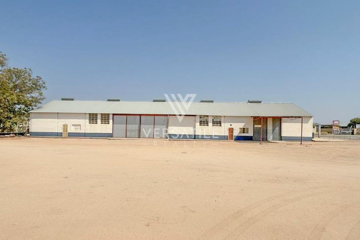 A wide-angle view of a large industrial warehouse building featuring corrugated metal roofing and multiple sliding access doors, set on a spacious dirt lot.