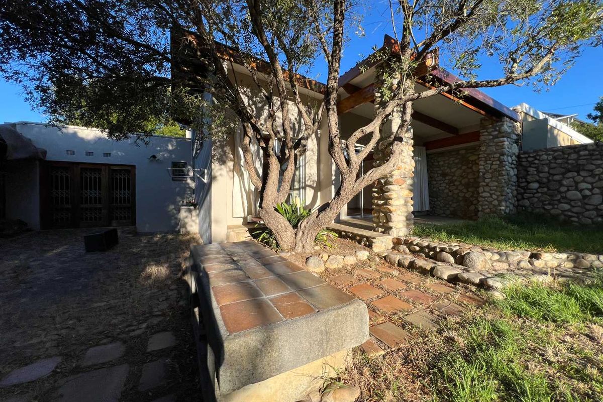 Rear exterior view featuring a stone-clad patio area with exposed timber beams, a built-in stone bench, and mature trees.