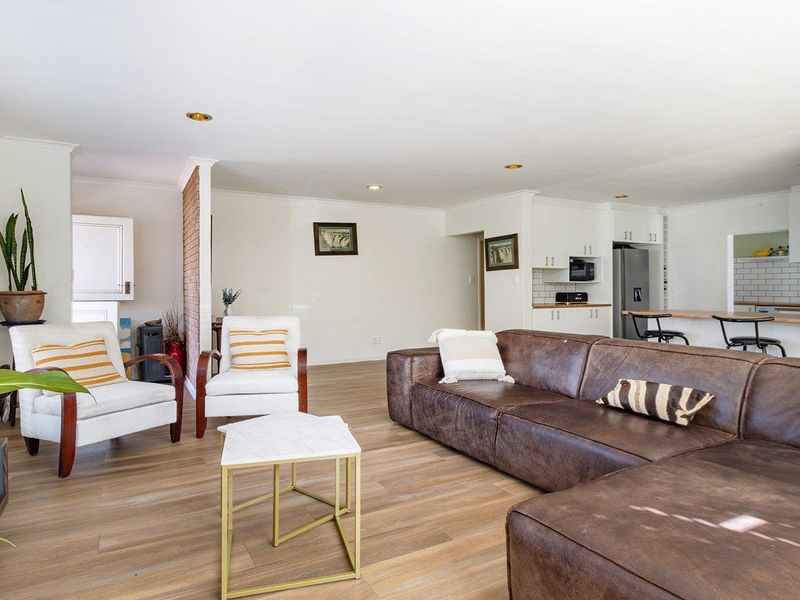 Spacious open-plan living area featuring modern laminate flooring, an exposed brick accent wall, and a functional kitchen with a breakfast bar and subway tiling.
