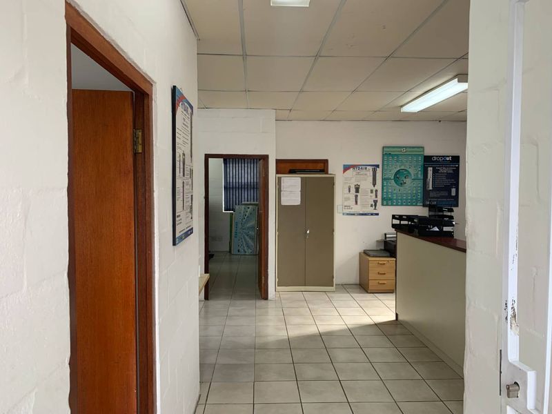 A functional office space featuring tiled flooring, a suspended ceiling, and a built-in reception counter, suitable for commercial or administrative use.