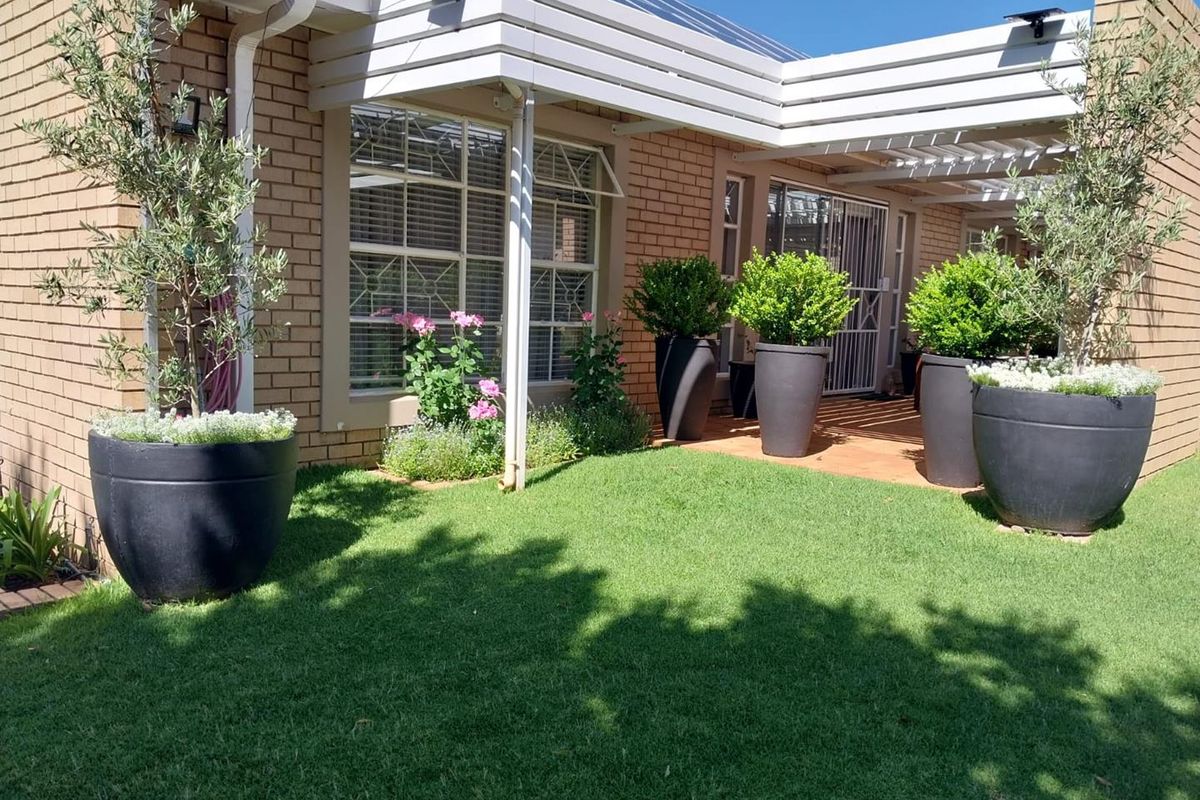 A well-maintained rear garden featuring a paved patio area, covered pergola, and brick exterior facade, offering a pleasant outdoor space.