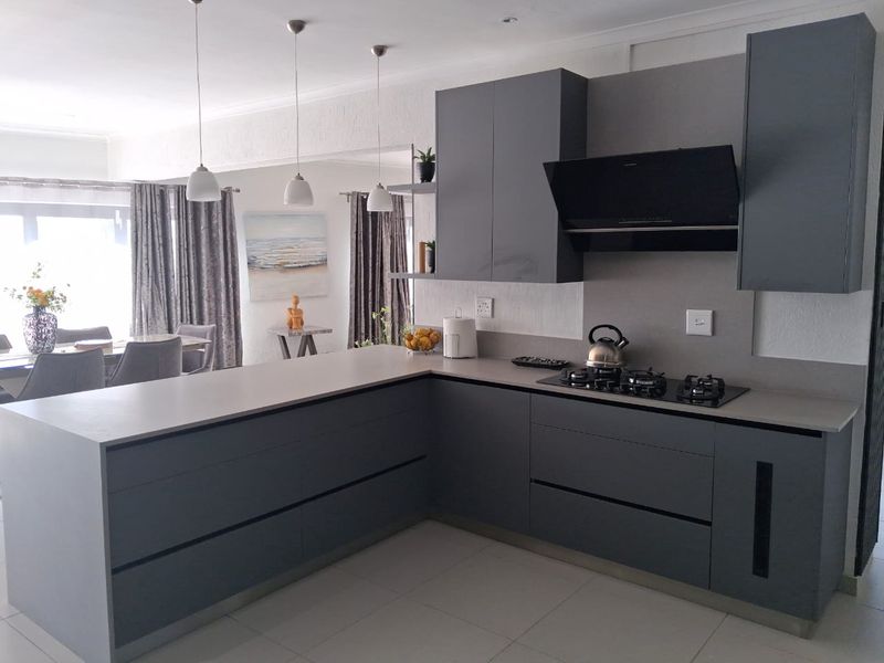 Modern open-plan kitchen featuring sleek grey cabinetry, stone countertops, a gas hob with extractor, and integrated pendant lighting, flowing into the dining area.