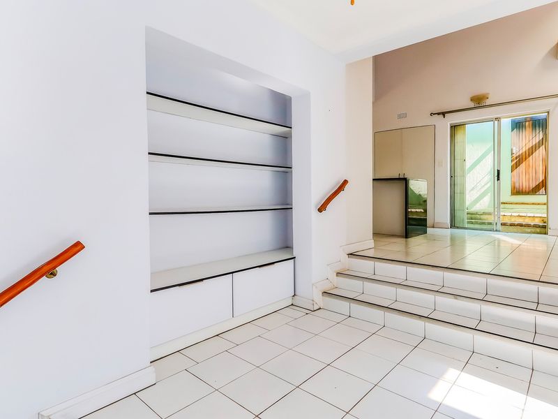 An open-plan living area featuring tiled flooring, built-in shelving, and a split-level design with access to an outdoor patio area.