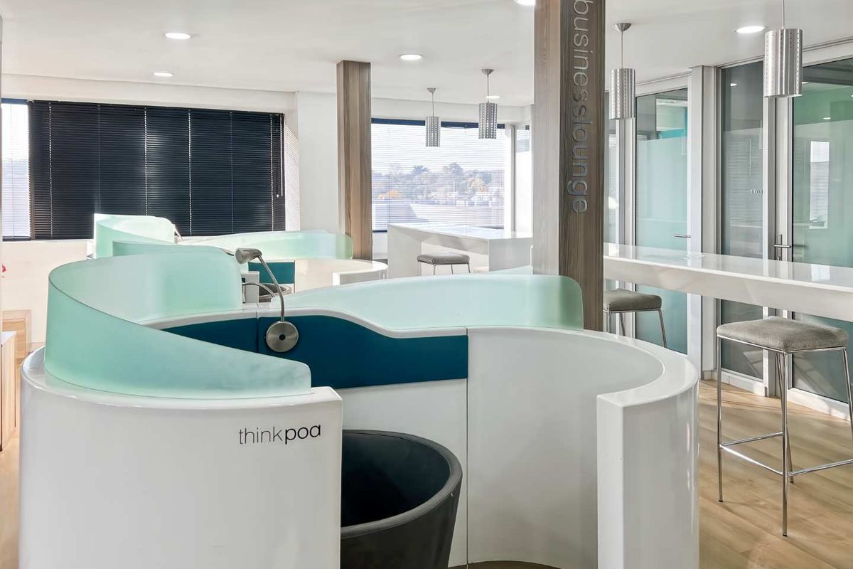 Modern office business lounge featuring curved privacy pods, integrated work counters, recessed lighting, and high-quality finishes throughout the professional workspace.