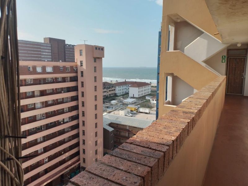 An elevated view from an apartment walkway overlooking the surrounding urban neighborhood and the distant coastline.
