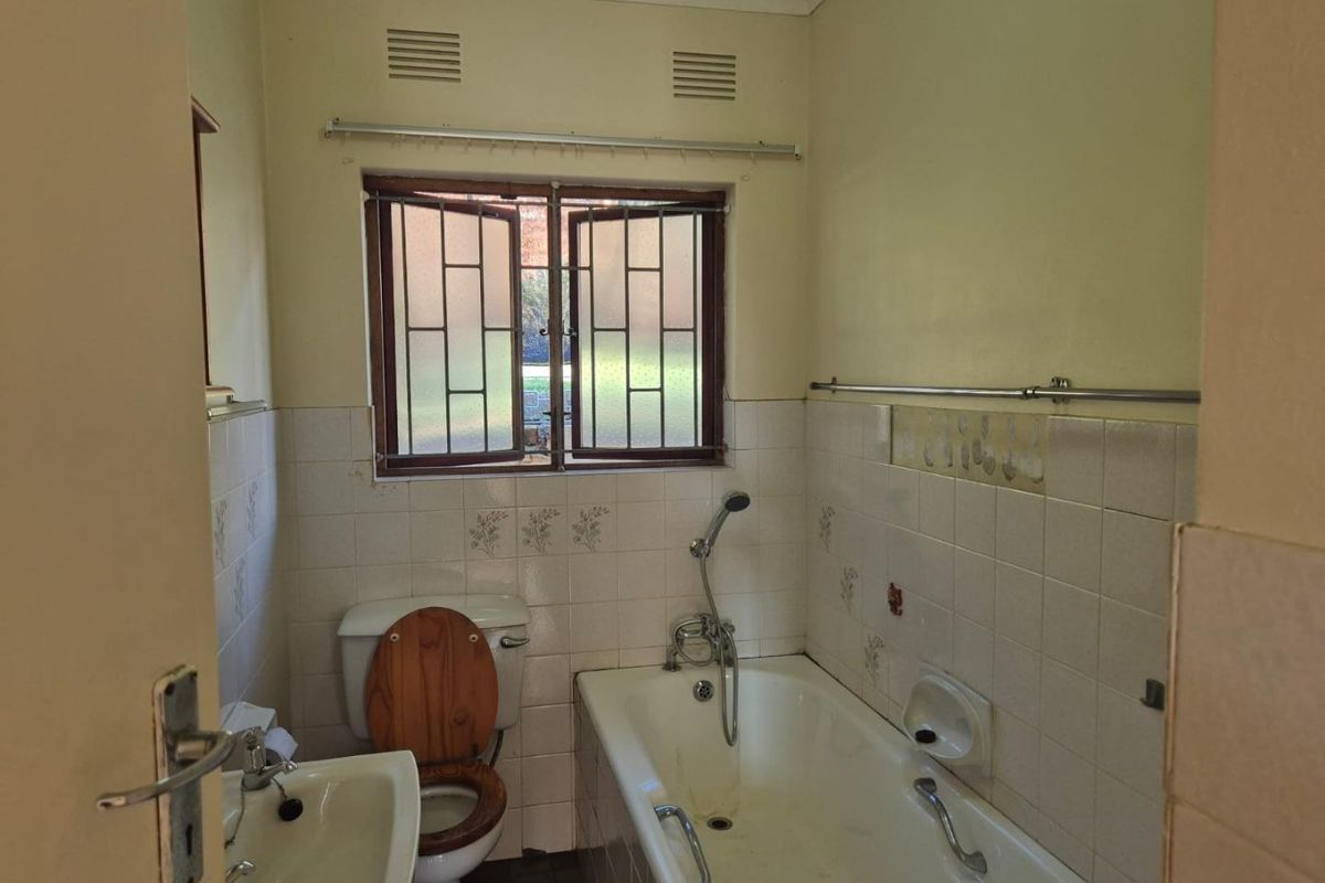 A dated bathroom featuring a bathtub with handheld shower, pedestal basin, and toilet, requiring cosmetic updates and tile repairs.