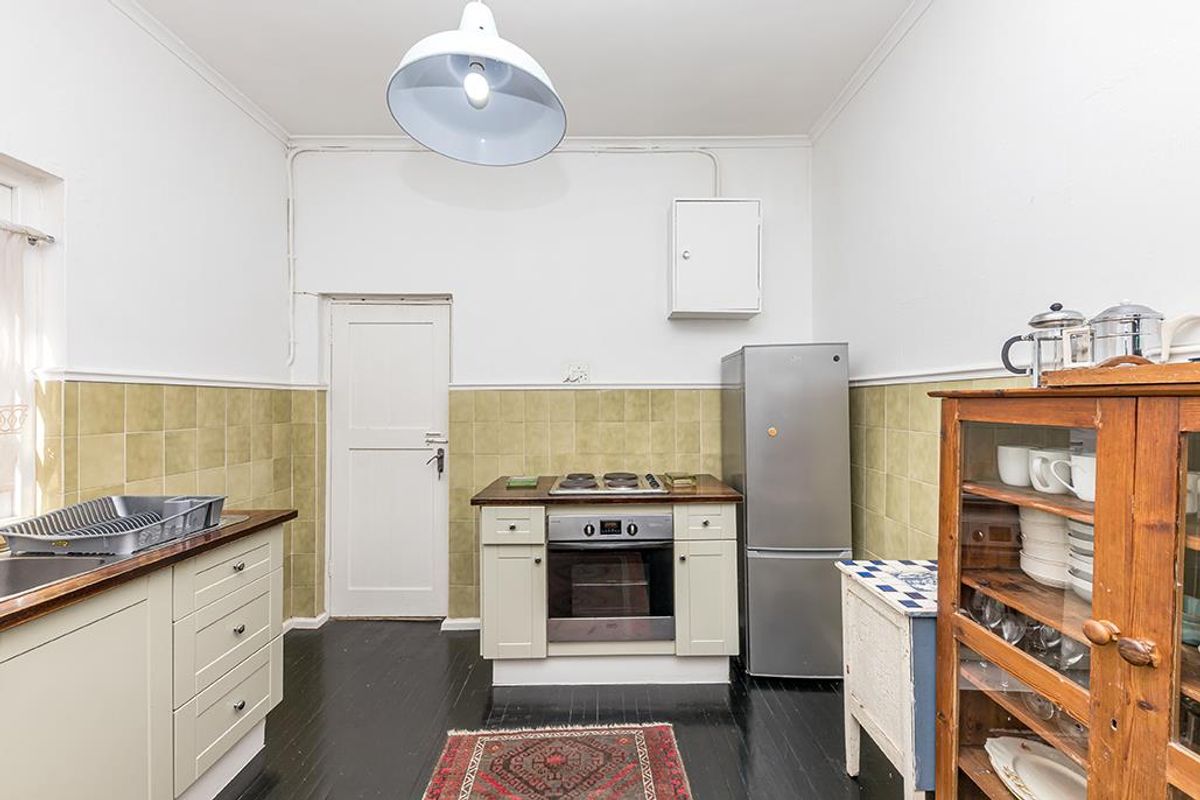 A functional kitchen featuring built-in cabinetry, a stainless steel oven and hob, tiled splashbacks, and a dark timber floor.