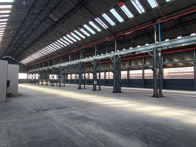 Spacious industrial warehouse featuring high ceilings with exposed steel trusses, abundant natural light from skylights, and durable concrete flooring.