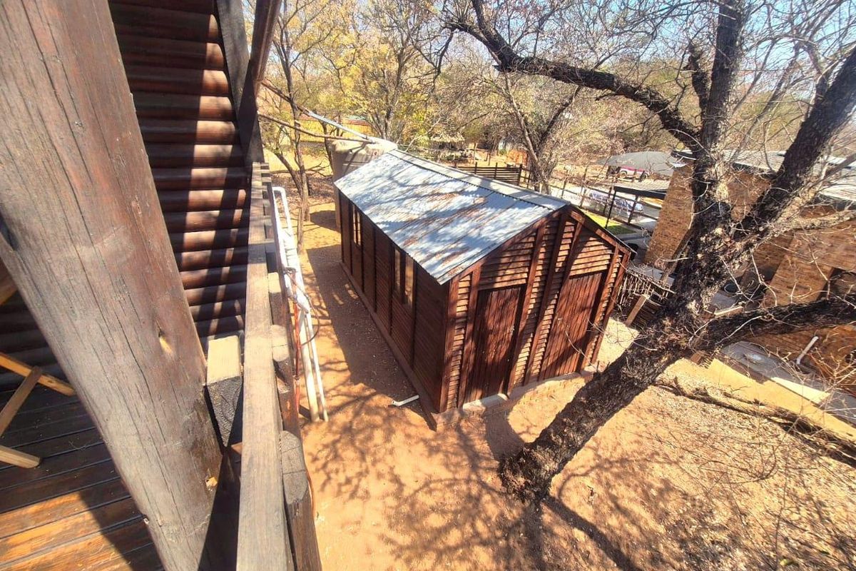 An elevated view of a detached timber outbuilding with a corrugated metal roof, situated in a wooded garden setting.