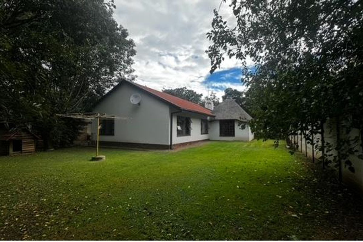 Rear view of the house featuring a spacious lawn, established trees, and a combination of pitched and thatched roof sections.