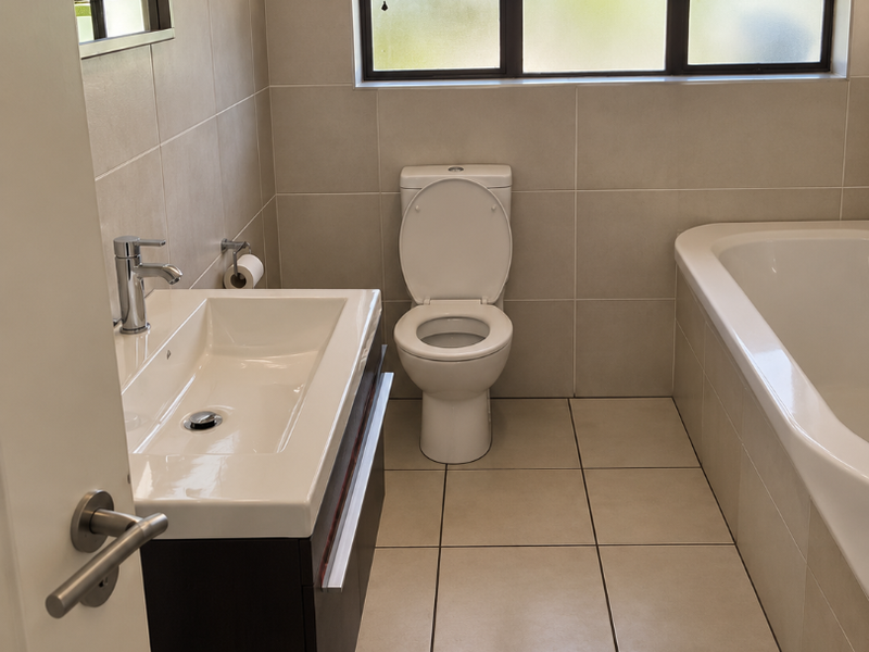 A modern, well-maintained bathroom featuring a vanity with basin, a toilet, and a bathtub, finished with neutral wall and floor tiles.