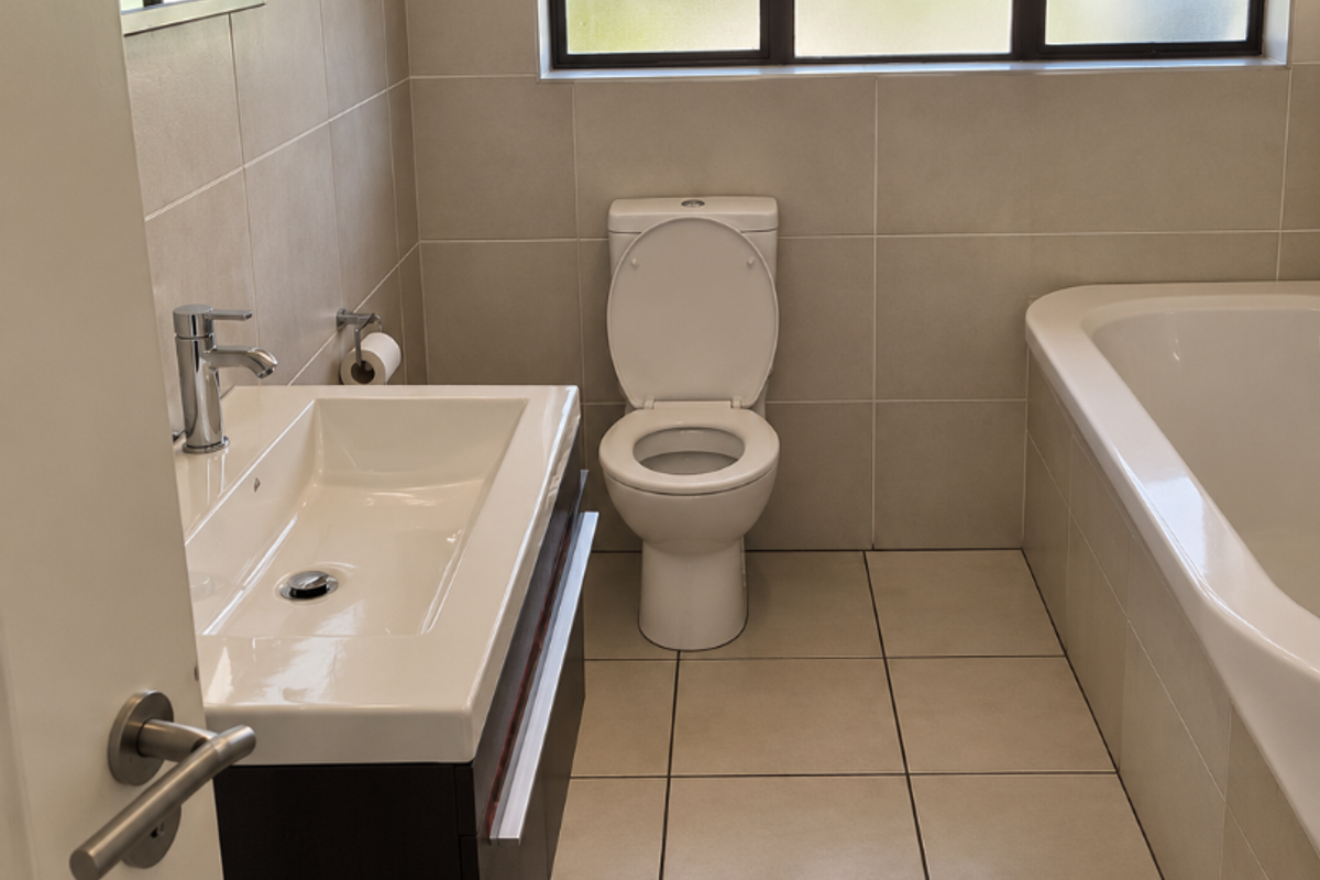 A modern, well-maintained bathroom featuring a vanity with basin, a toilet, and a bathtub, finished with neutral wall and floor tiles.