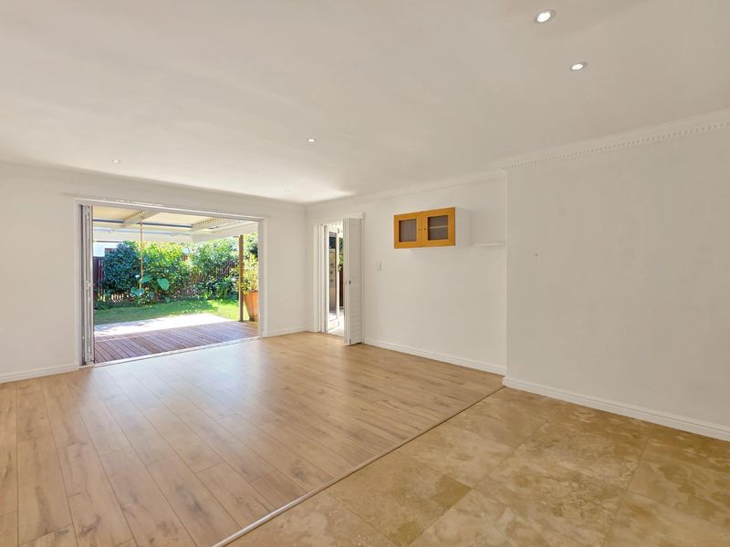 Spacious open-plan living area featuring a mix of timber laminate and travertine flooring, recessed lighting, and seamless access to an outdoor patio.