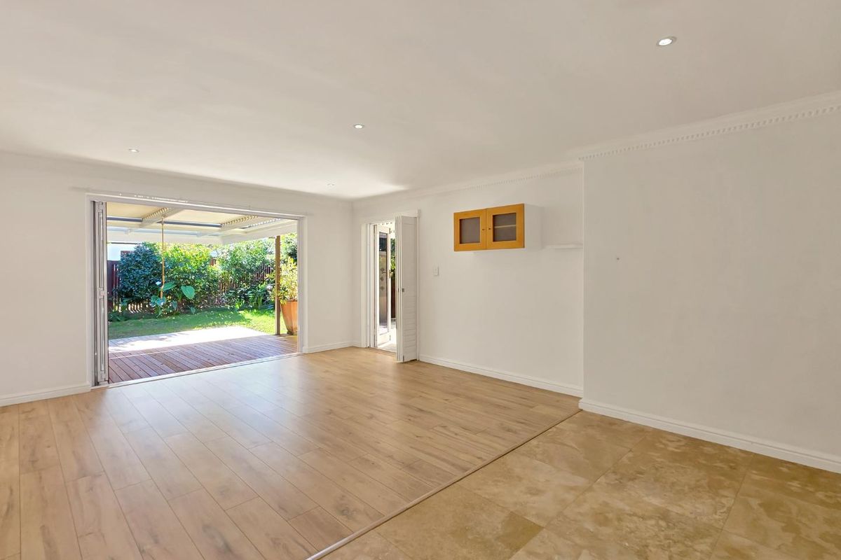 Spacious open-plan living area featuring a mix of timber laminate and travertine flooring, recessed lighting, and seamless access to an outdoor patio.